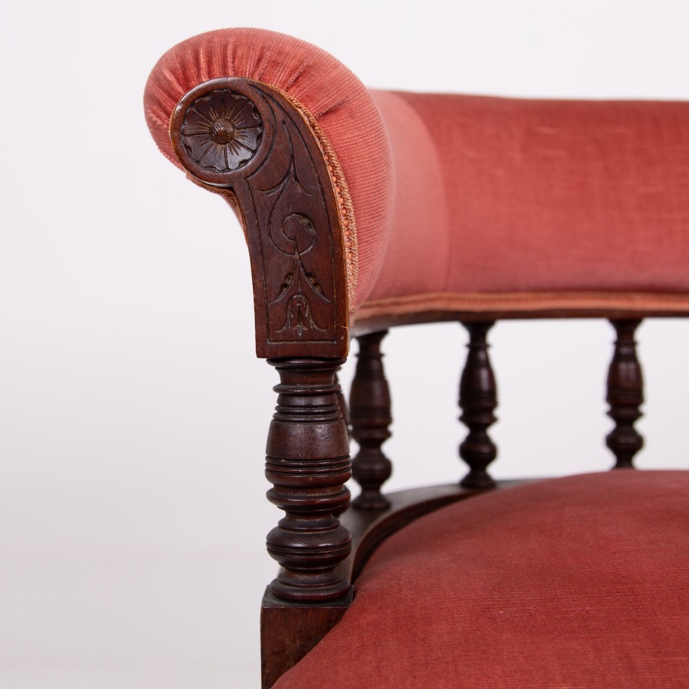 A late Victorian armchair featuring a curved horseshoe back rest, turned wood spindles, terracotta fabric upholstery, and turned front legs on castors. View VIII