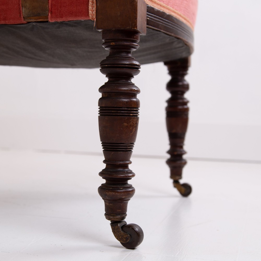 A late Victorian armchair featuring a curved horseshoe back rest, turned wood spindles, terracotta fabric upholstery, and turned front legs on castors. View IX