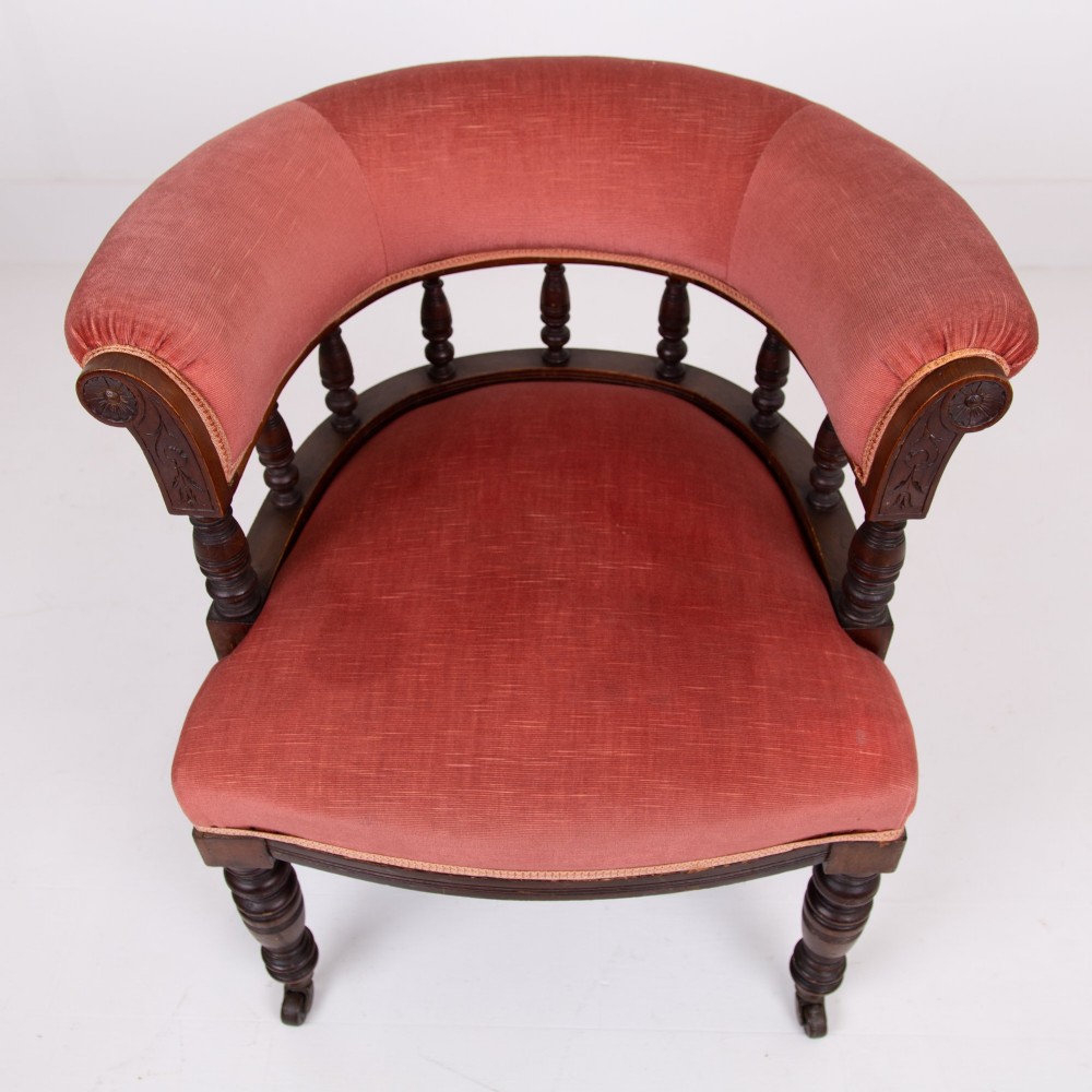 A late Victorian armchair featuring a curved horseshoe back rest, turned wood spindles, terracotta fabric upholstery, and turned front legs on castors. View XI