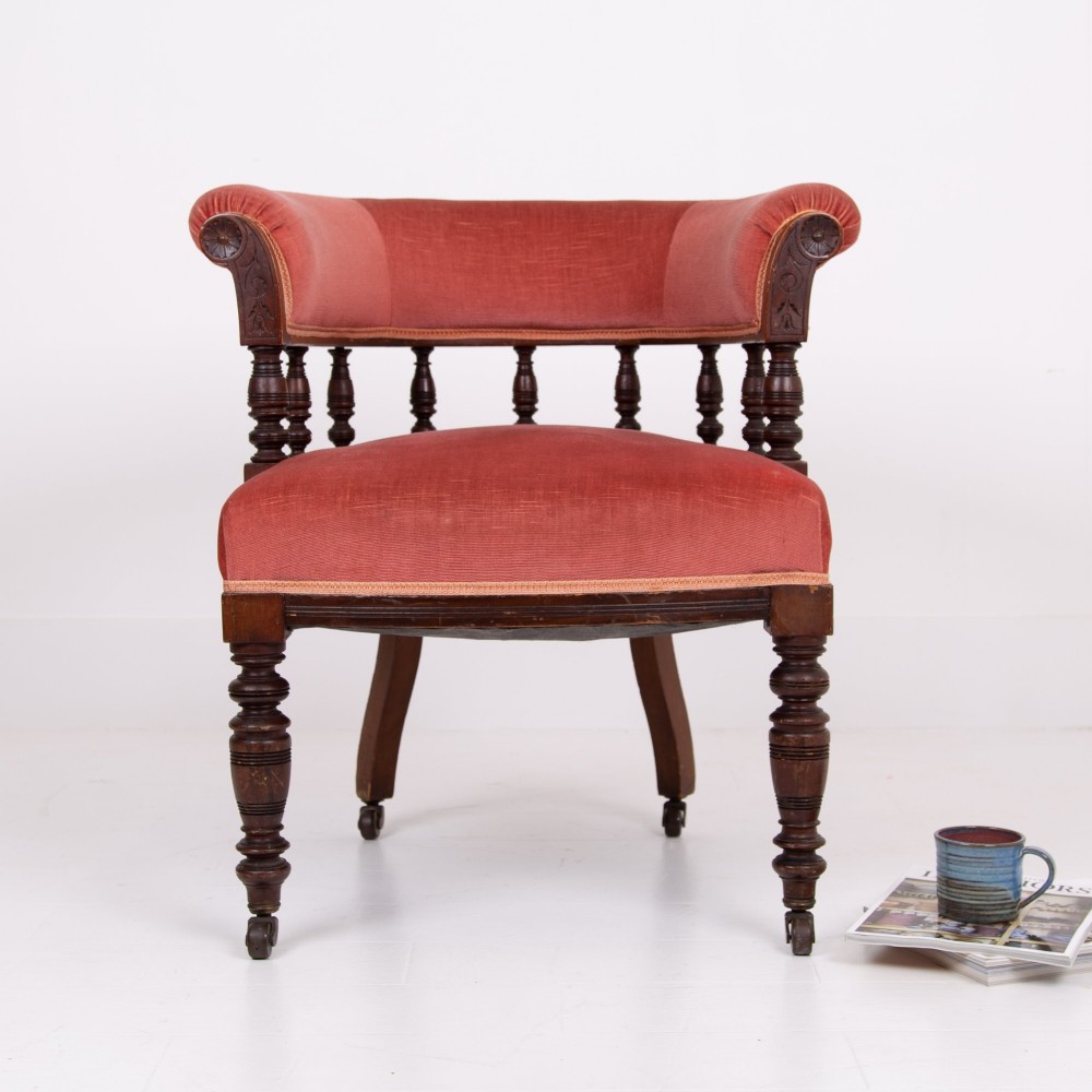 A late Victorian armchair featuring a curved horseshoe back rest, turned wood spindles, terracotta fabric upholstery, and turned front legs on castors. View XII
