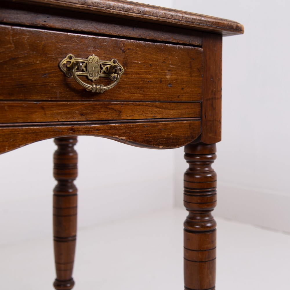 A brown walnut writing desk featuring two frieze drawers with brass handles, turned legs, and a rectangular inset leather top. View V