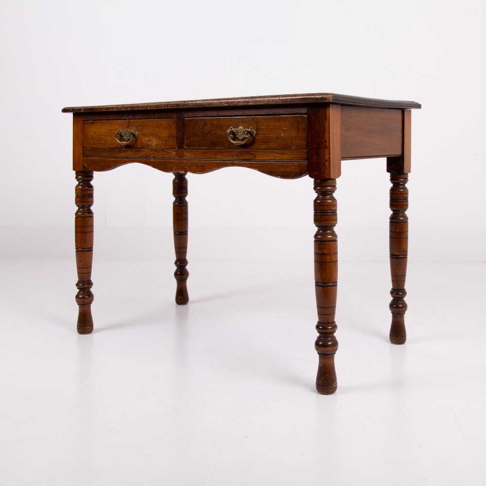 A brown walnut writing desk featuring two frieze drawers with brass handles, turned legs, and a rectangular inset leather top. View X