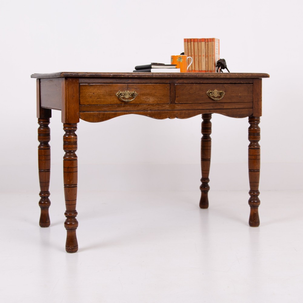 A brown walnut writing desk featuring two frieze drawers with brass handles, turned legs, and a rectangular inset leather top. View XII