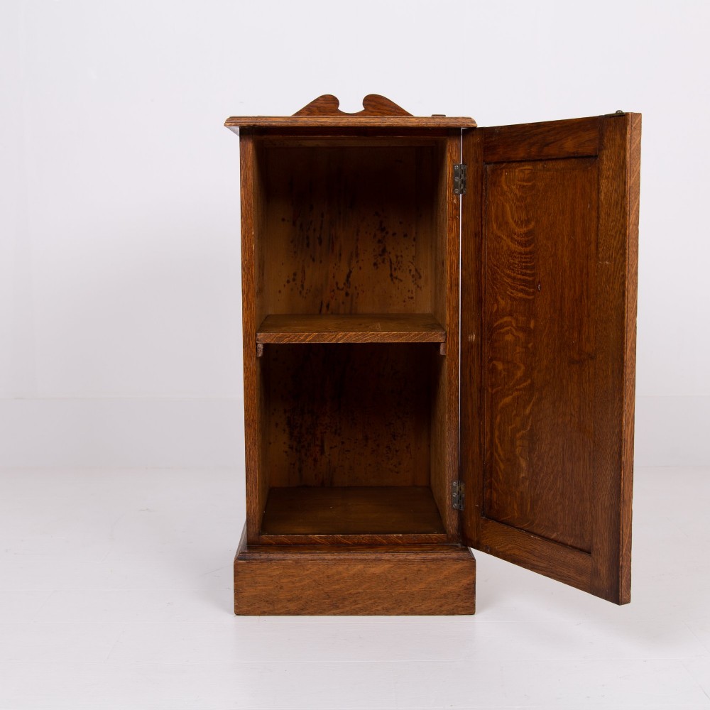 A slim Victorian oak pot cupboard featuring a single panelled door with a small brass latch, resting on a solid plinth base with a gallery top. View III