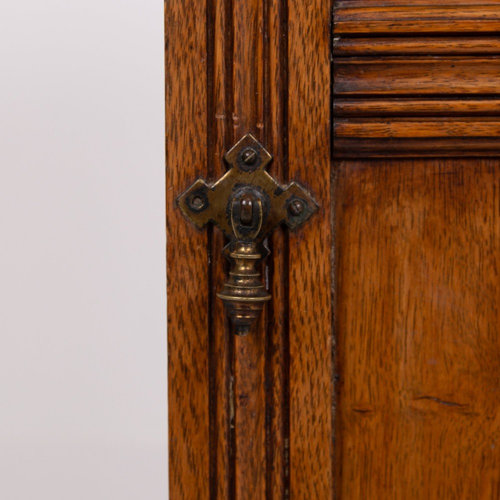 A slim Victorian oak pot cupboard featuring a single panelled door with a small brass latch, resting on a solid plinth base with a gallery top. View VIII