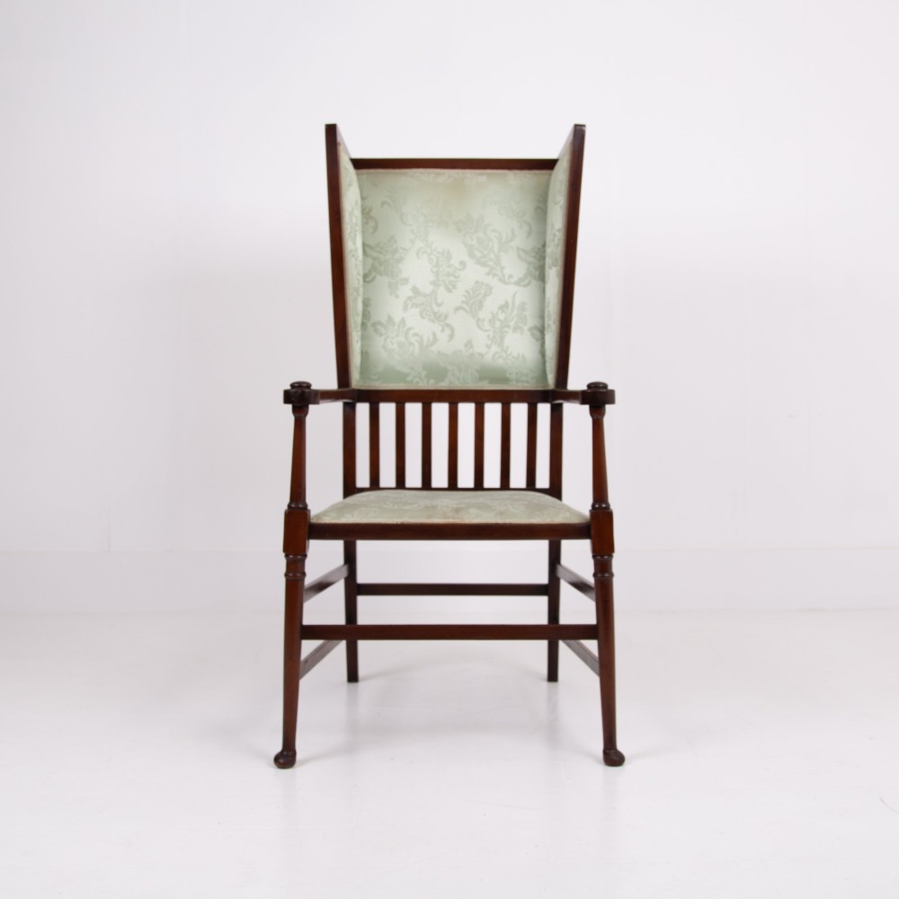 An Arts and Crafts high-backed armchair crafted from dark timber with vertical under-arm slats, architectural wings, and pale green patterned fabric upholstery. View II