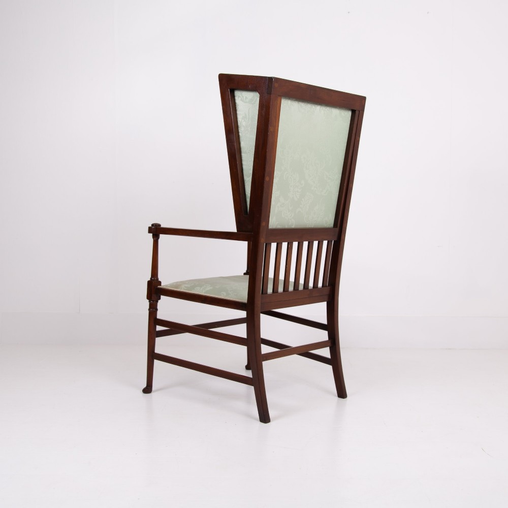 An Arts and Crafts high-backed armchair crafted from dark timber with vertical under-arm slats, architectural wings, and pale green patterned fabric upholstery. View III
