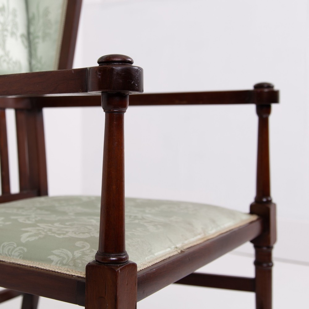 An Arts and Crafts high-backed armchair crafted from dark timber with vertical under-arm slats, architectural wings, and pale green patterned fabric upholstery. View IV