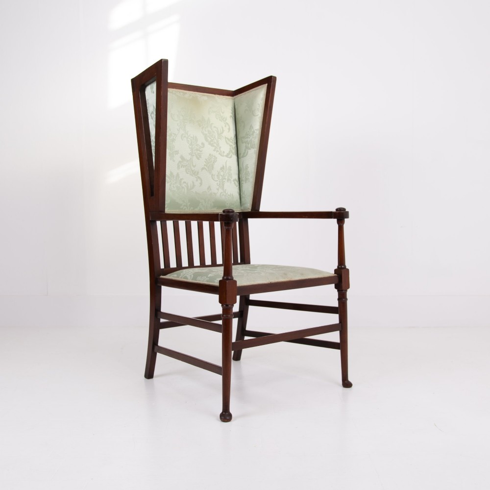 An Arts and Crafts high-backed armchair crafted from dark timber with vertical under-arm slats, architectural wings, and pale green patterned fabric upholstery. View V