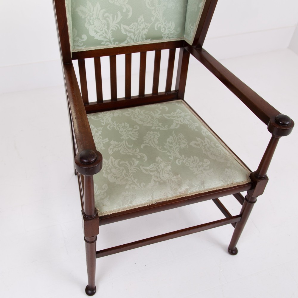 An Arts and Crafts high-backed armchair crafted from dark timber with vertical under-arm slats, architectural wings, and pale green patterned fabric upholstery. View IX