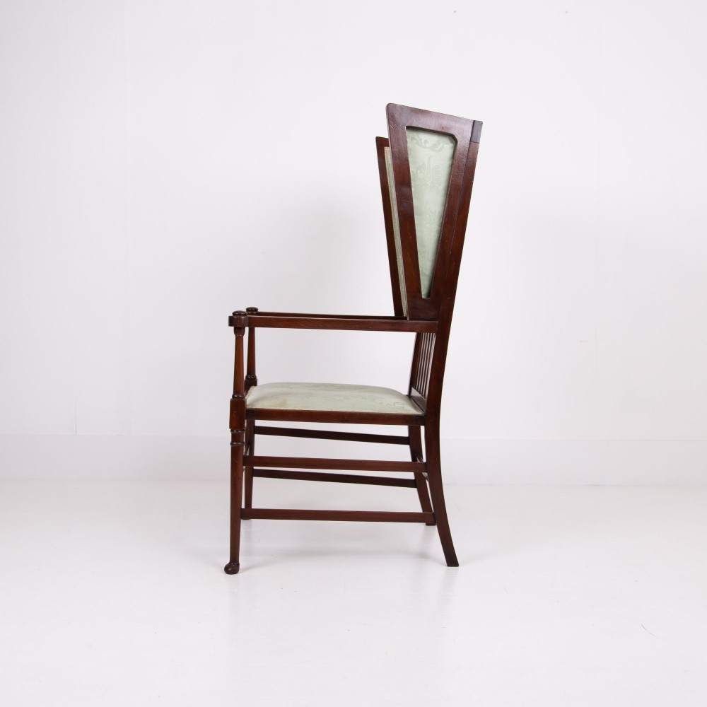 An Arts and Crafts high-backed armchair crafted from dark timber with vertical under-arm slats, architectural wings, and pale green patterned fabric upholstery. View XI