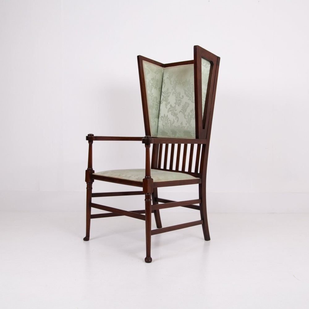 An Arts and Crafts high-backed armchair crafted from dark timber with vertical under-arm slats, architectural wings, and pale green patterned fabric upholstery. View XII