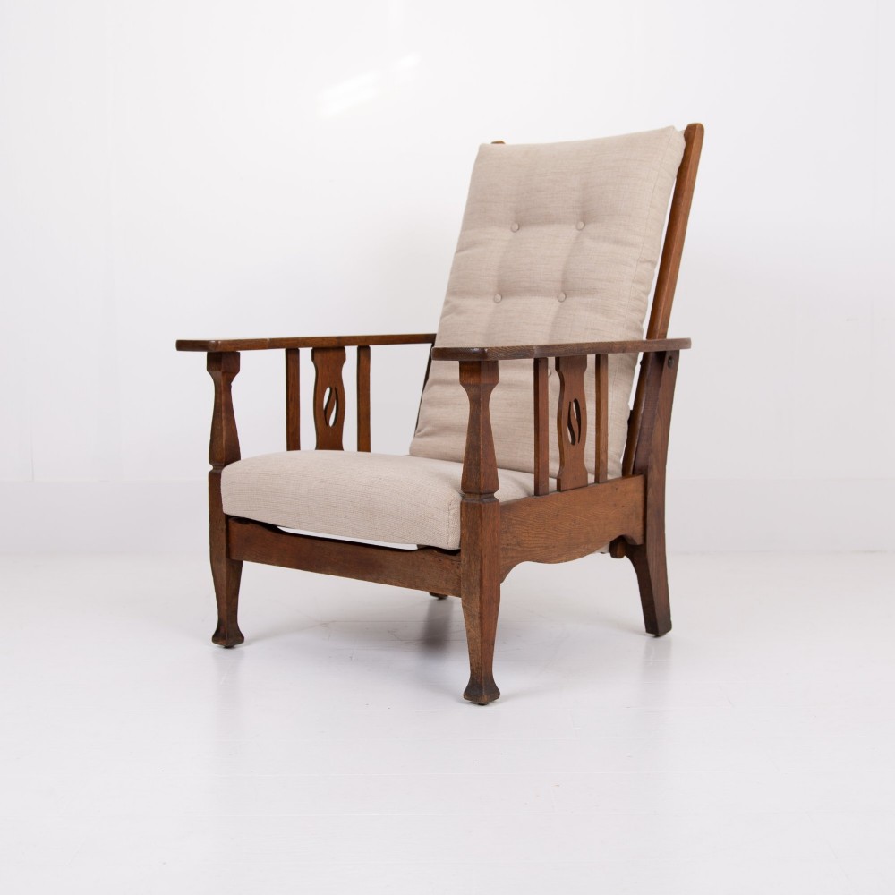 An Arts and Crafts oak reclining armchair featuring a beige buttoned cushion and pierced side splats.