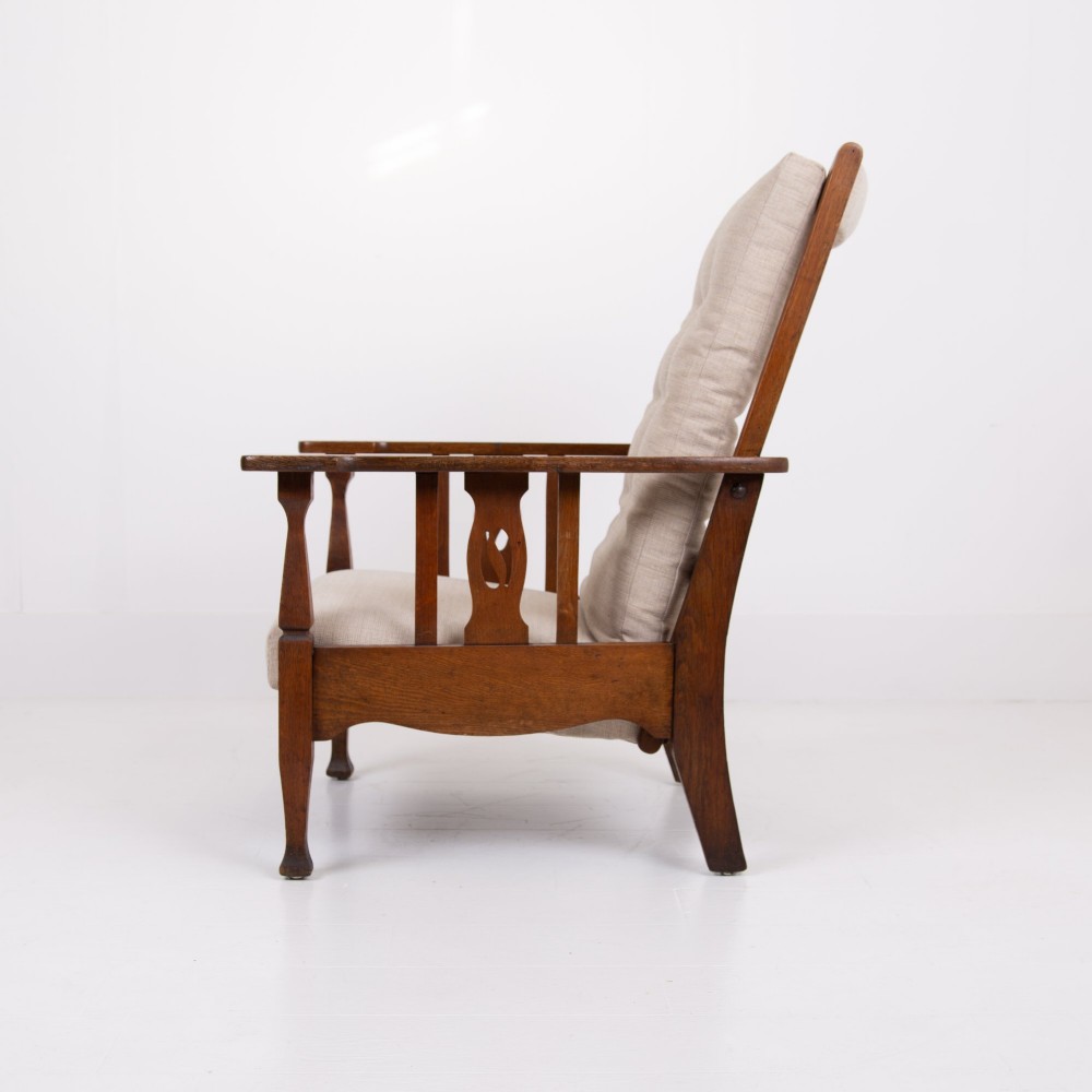 An Arts and Crafts oak reclining armchair featuring a beige buttoned cushion and pierced side splats. View III