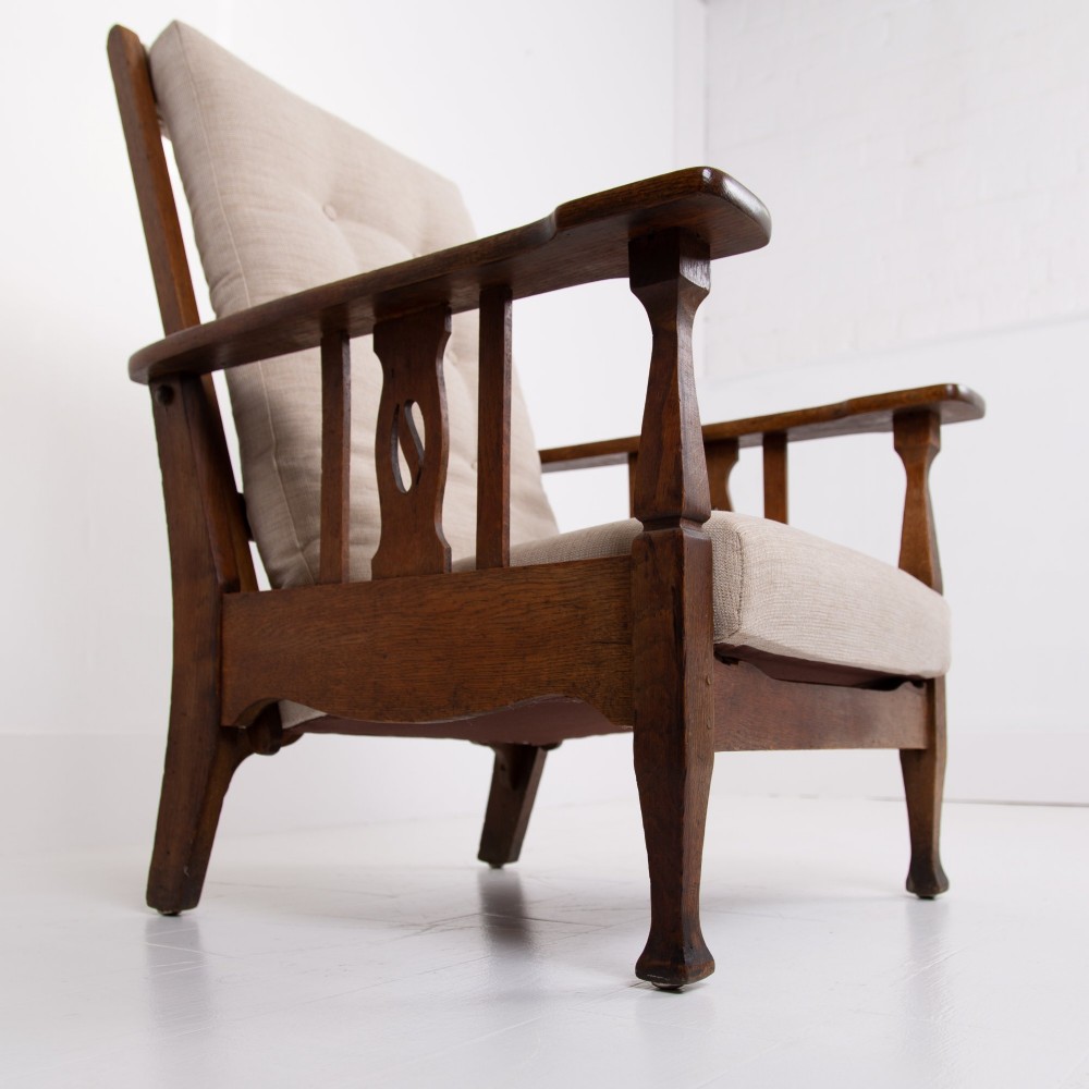 An Arts and Crafts oak reclining armchair featuring a beige buttoned cushion and pierced side splats. View IV