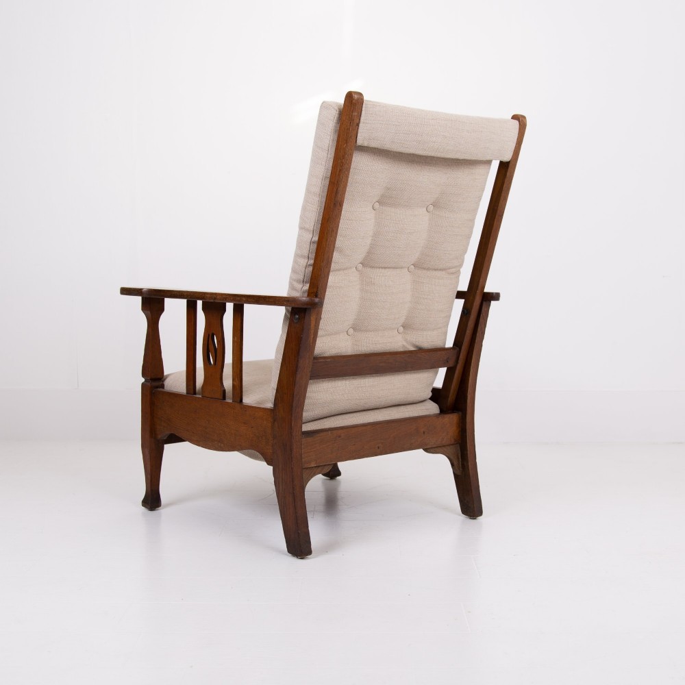 An Arts and Crafts oak reclining armchair featuring a beige buttoned cushion and pierced side splats. View VIII