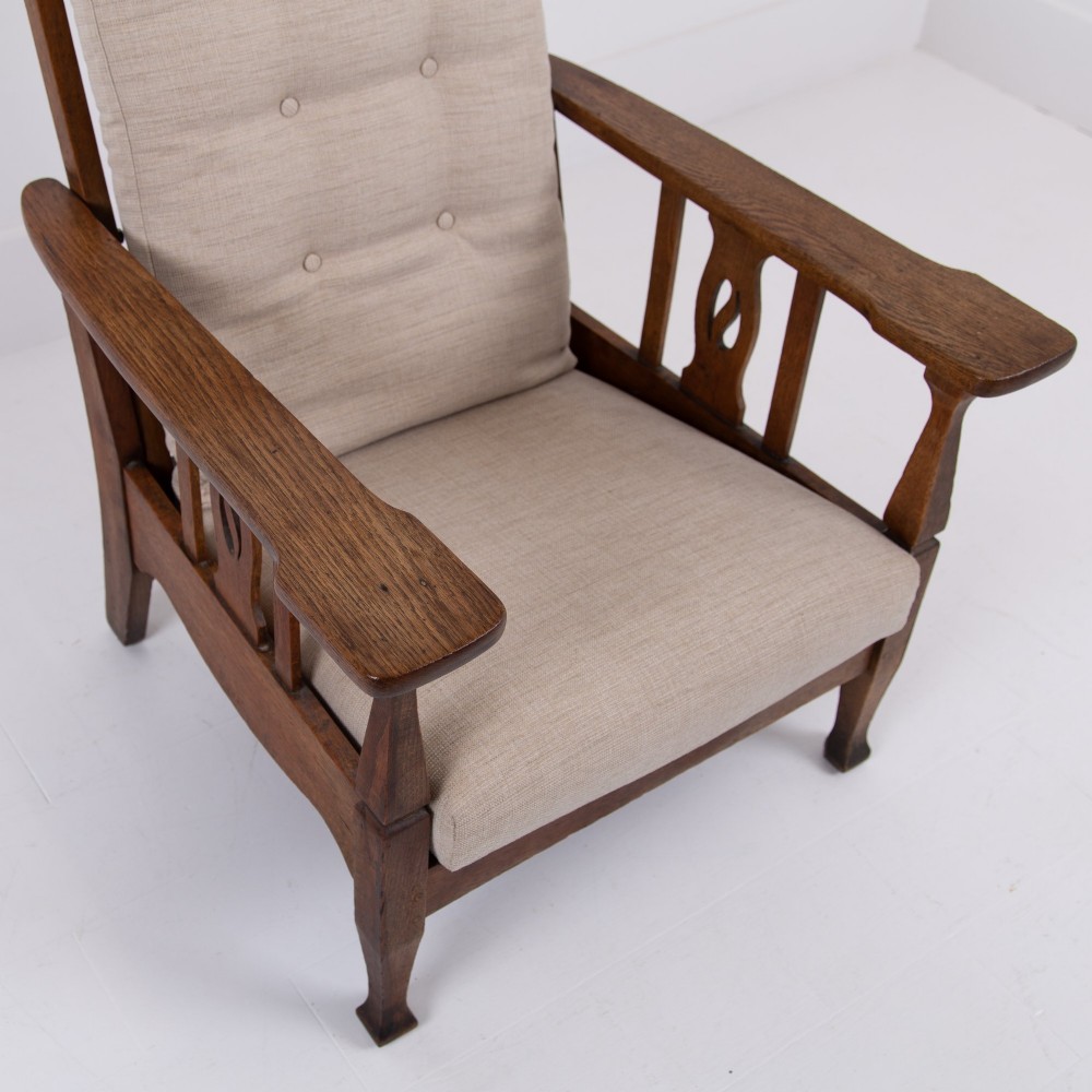 An Arts and Crafts oak reclining armchair featuring a beige buttoned cushion and pierced side splats. View X