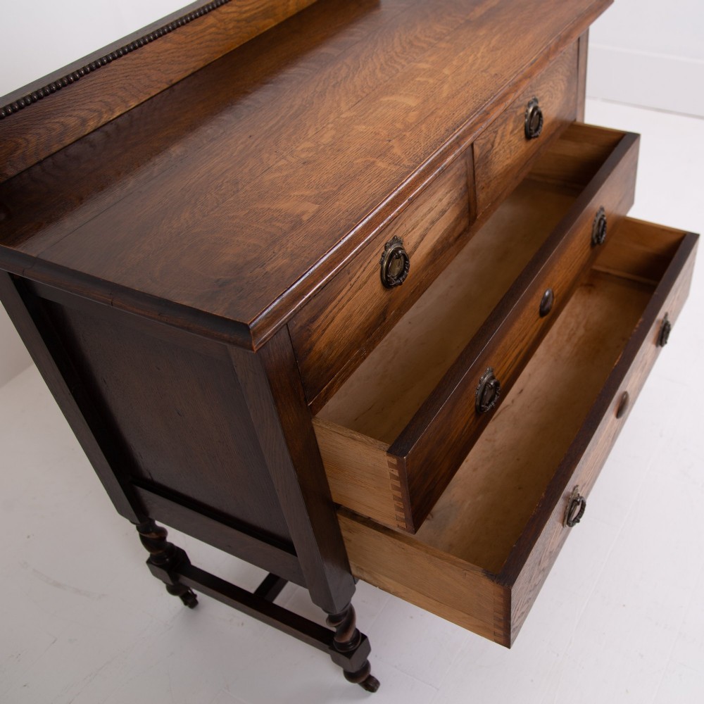 An Edwardian oak chest of drawers with two short over two long drawers, brass drop handles, a low backstand, and barley twist legs set on castors. View IV