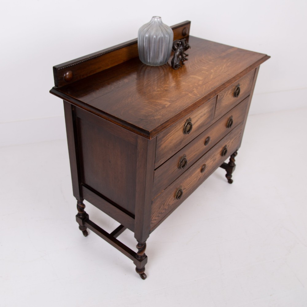 An Edwardian oak chest of drawers with two short over two long drawers, brass drop handles, a low backstand, and barley twist legs set on castors. View V