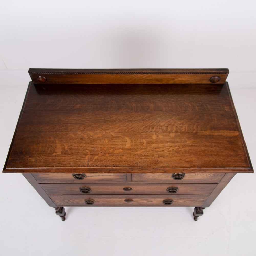 An Edwardian oak chest of drawers with two short over two long drawers, brass drop handles, a low backstand, and barley twist legs set on castors. View VI