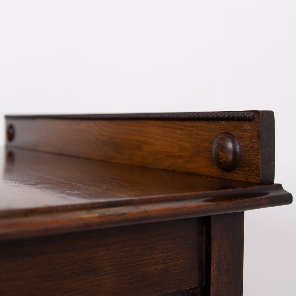 An Edwardian oak chest of drawers with two short over two long drawers, brass drop handles, a low backstand, and barley twist legs set on castors. View XI