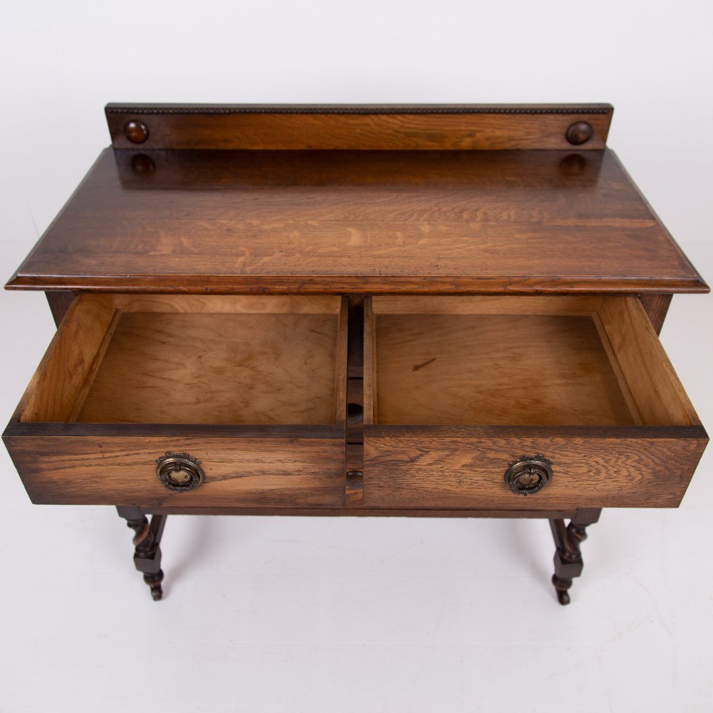 An Edwardian oak chest of drawers with two short over two long drawers, brass drop handles, a low backstand, and barley twist legs set on castors. View XII