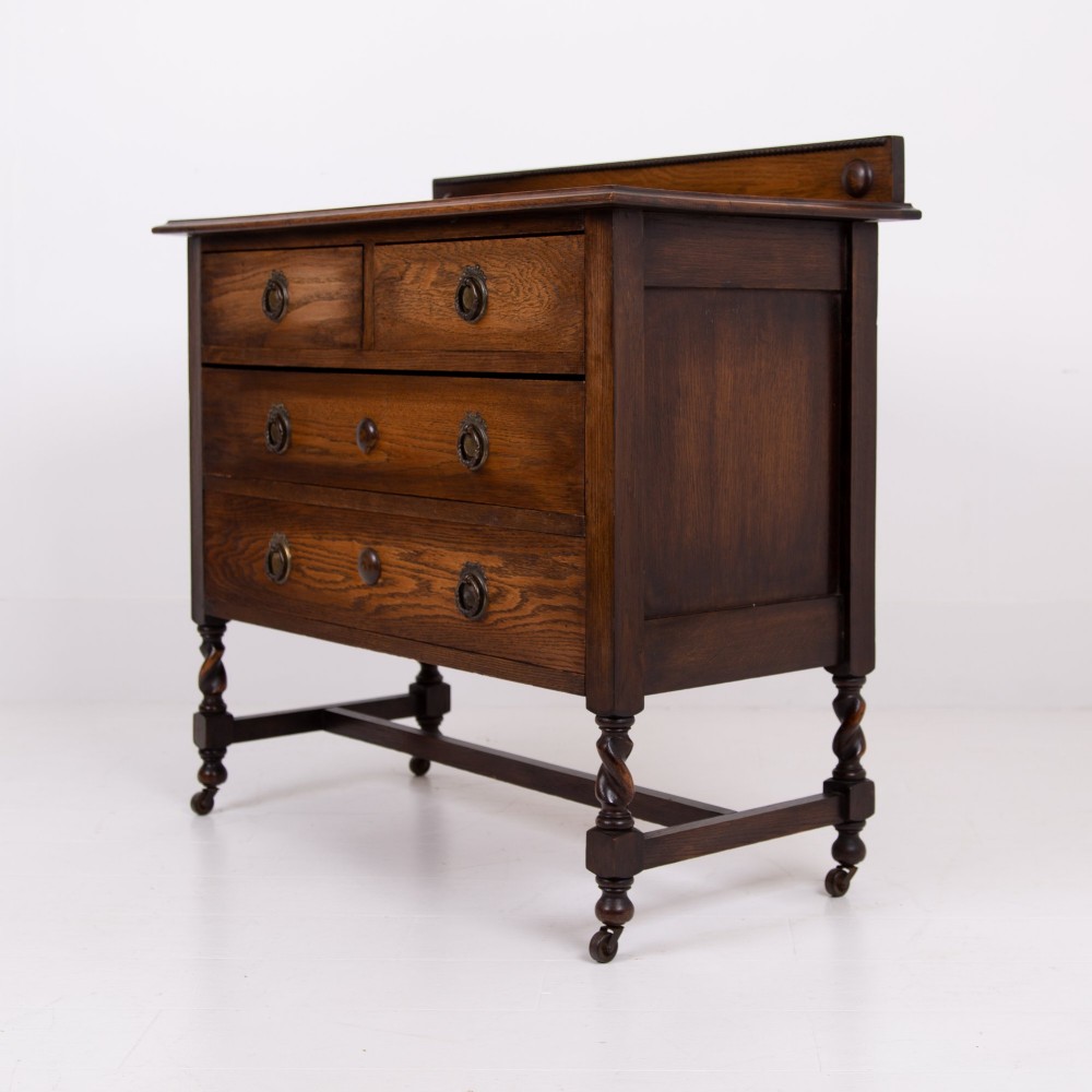 An Edwardian oak chest of drawers with two short over two long drawers, brass drop handles, a low backstand, and barley twist legs set on castors. View XIII