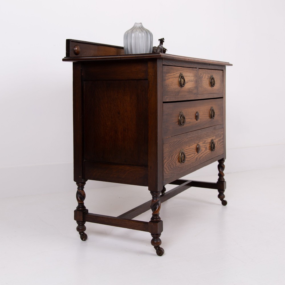 An Edwardian oak chest of drawers with two short over two long drawers, brass drop handles, a low backstand, and barley twist legs set on castors. View XV