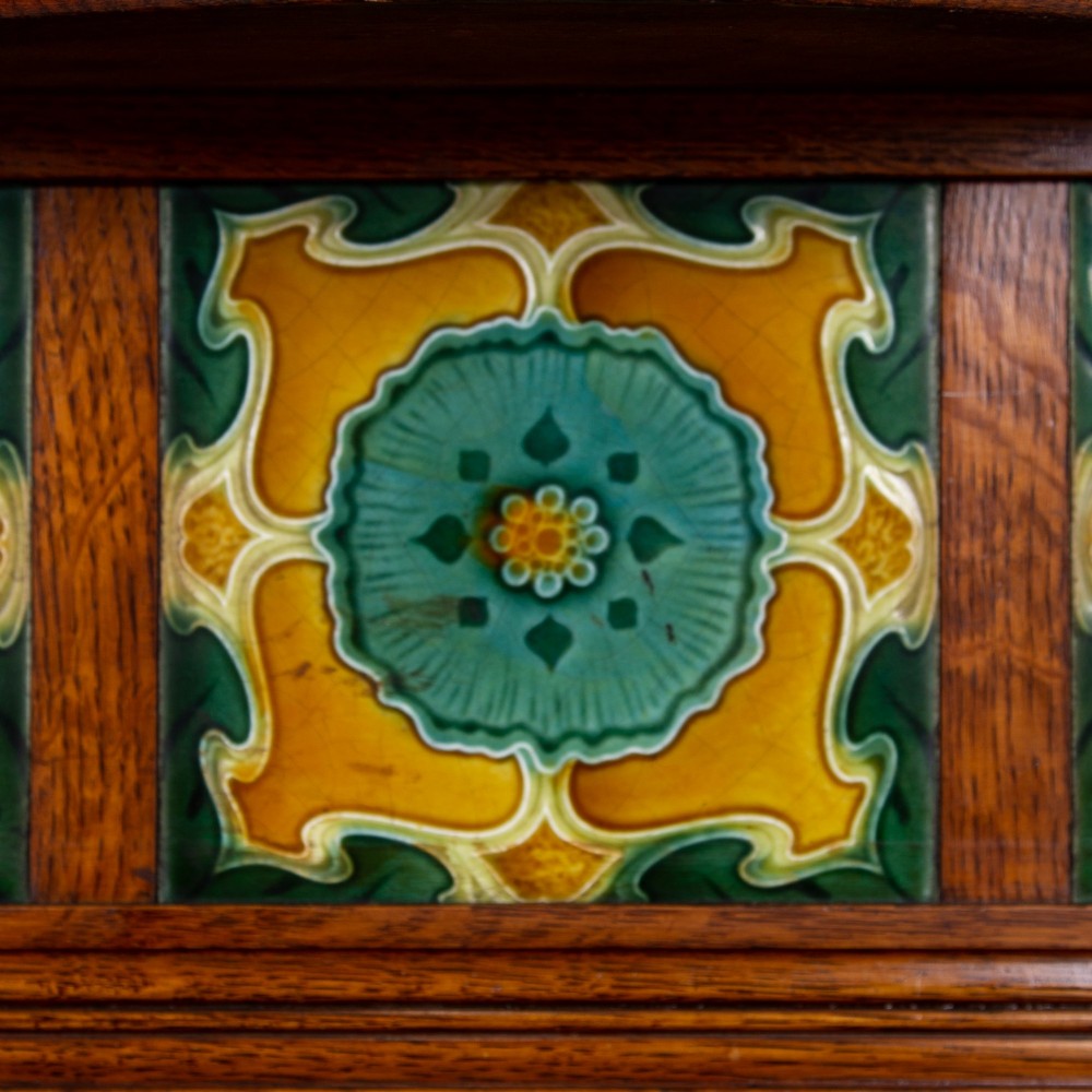 A tall Victorian golden oak hallstand featuring an octagonal central mirror, decorative ceramic tiles, brass coat hooks, a single central drawer, and lower umbrella drip trays. View III