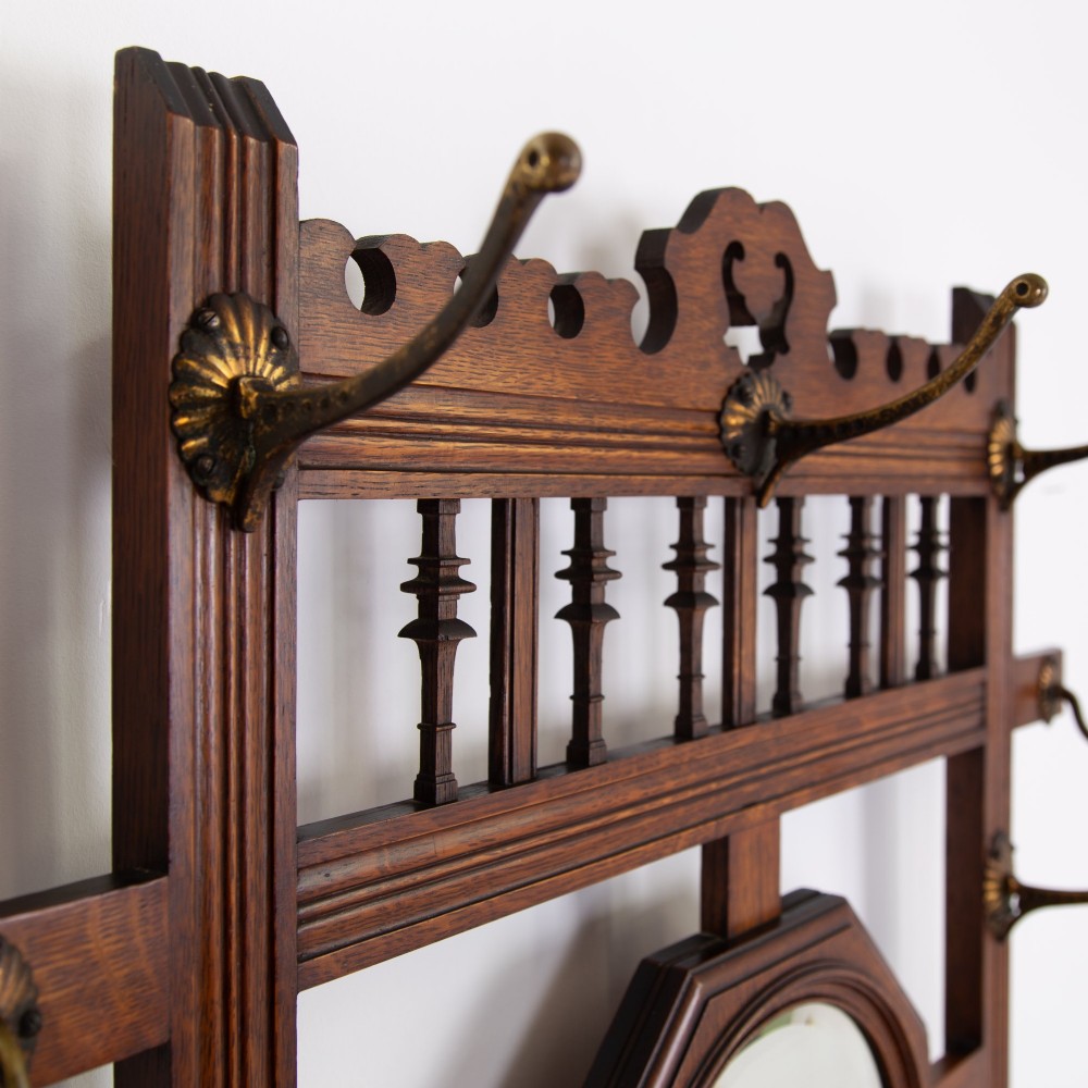 A tall Victorian golden oak hallstand featuring an octagonal central mirror, decorative ceramic tiles, brass coat hooks, a single central drawer, and lower umbrella drip trays. View IV