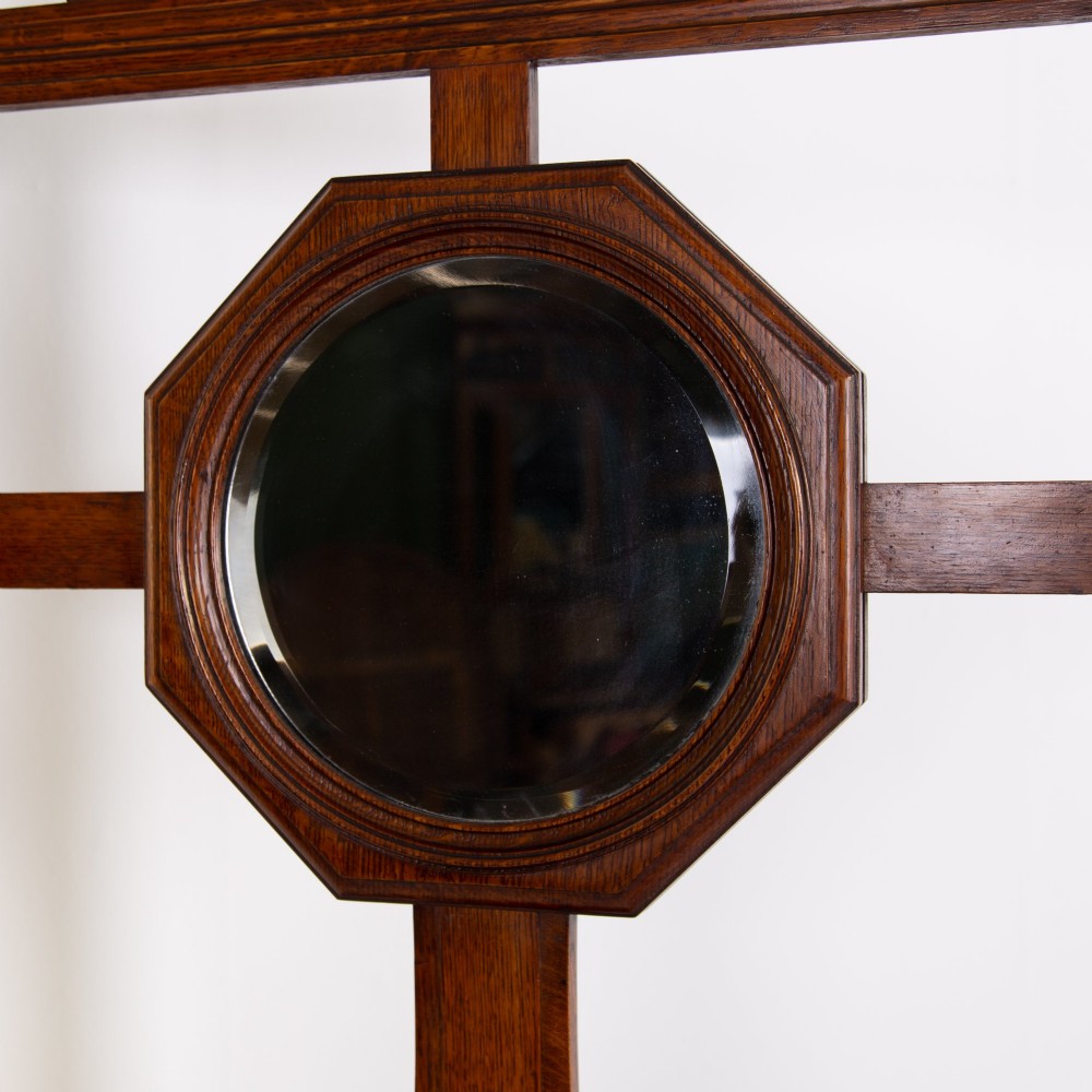 A tall Victorian golden oak hallstand featuring an octagonal central mirror, decorative ceramic tiles, brass coat hooks, a single central drawer, and lower umbrella drip trays. View V
