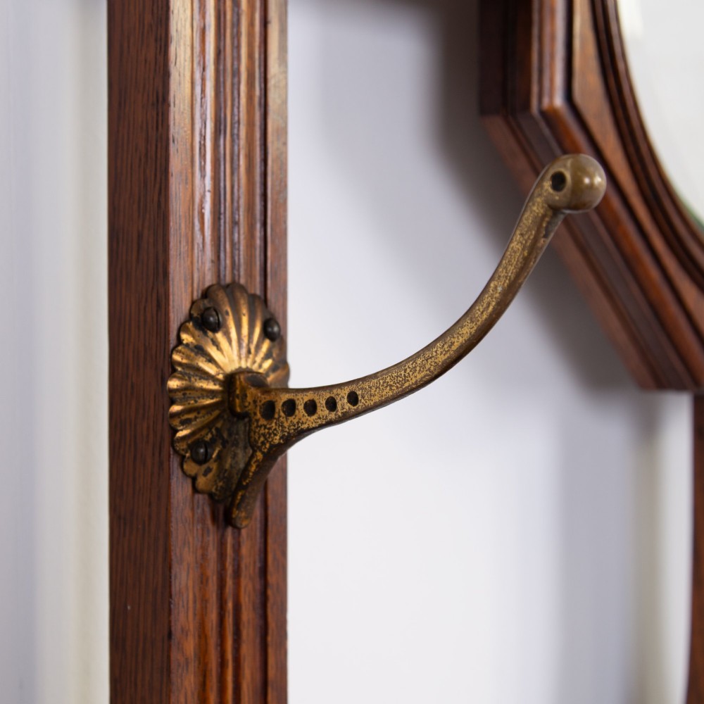 A tall Victorian golden oak hallstand featuring an octagonal central mirror, decorative ceramic tiles, brass coat hooks, a single central drawer, and lower umbrella drip trays. View VI