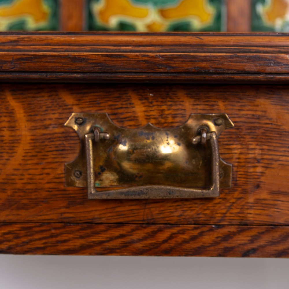 A tall Victorian golden oak hallstand featuring an octagonal central mirror, decorative ceramic tiles, brass coat hooks, a single central drawer, and lower umbrella drip trays. View VIII