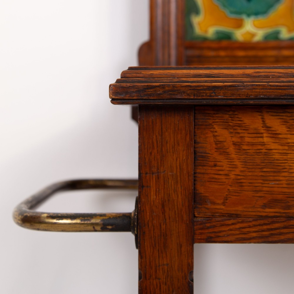 A tall Victorian golden oak hallstand featuring an octagonal central mirror, decorative ceramic tiles, brass coat hooks, a single central drawer, and lower umbrella drip trays. View XIII