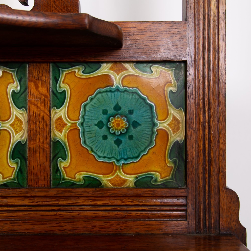A tall Victorian golden oak hallstand featuring an octagonal central mirror, decorative ceramic tiles, brass coat hooks, a single central drawer, and lower umbrella drip trays. View XV