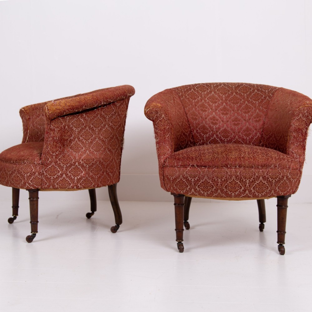 A pair of 19th-century Victorian tub armchairs upholstered in patterned red fabric with turned wooden legs on brass castors.