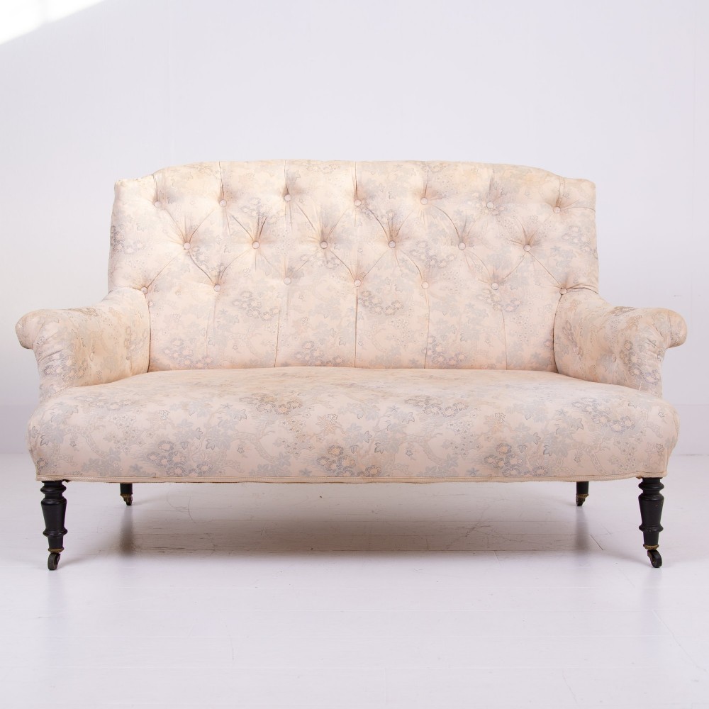 An antique French Napoleon III sofa upholstered in pale cream patterned fabric with deep buttoning, curved backrest, and turned dark wooden legs on brass castors. View III