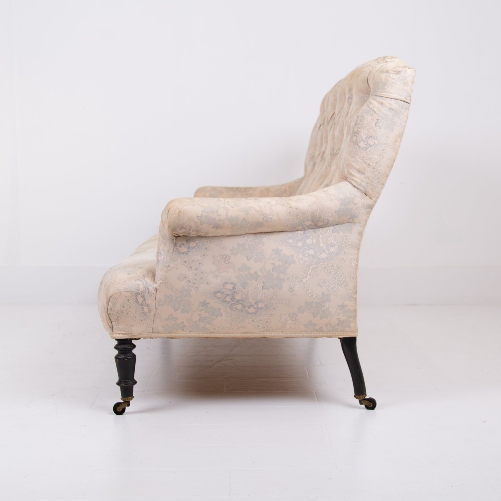 An antique French Napoleon III sofa upholstered in pale cream patterned fabric with deep buttoning, curved backrest, and turned dark wooden legs on brass castors. View IV