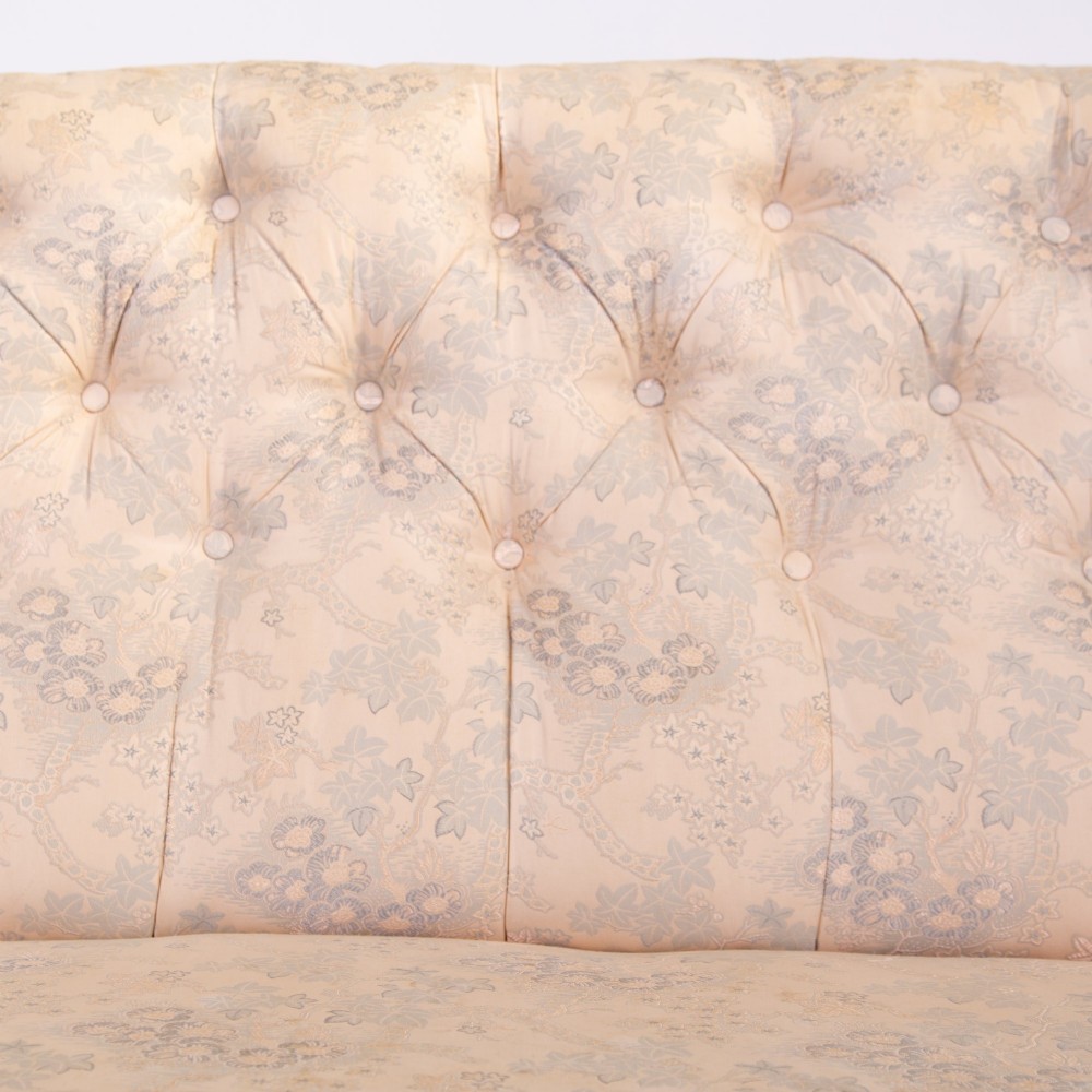 An antique French Napoleon III sofa upholstered in pale cream patterned fabric with deep buttoning, curved backrest, and turned dark wooden legs on brass castors. View V