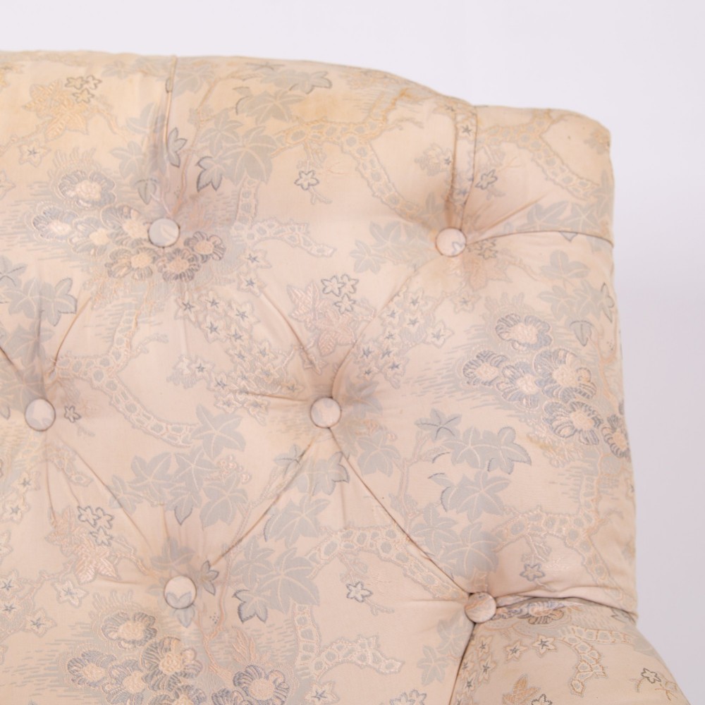 An antique French Napoleon III sofa upholstered in pale cream patterned fabric with deep buttoning, curved backrest, and turned dark wooden legs on brass castors. View VI