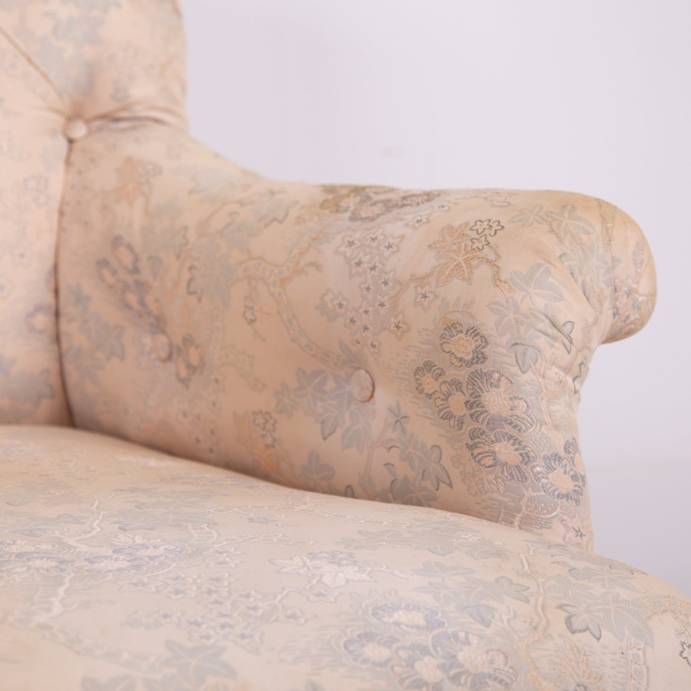 An antique French Napoleon III sofa upholstered in pale cream patterned fabric with deep buttoning, curved backrest, and turned dark wooden legs on brass castors. View VII