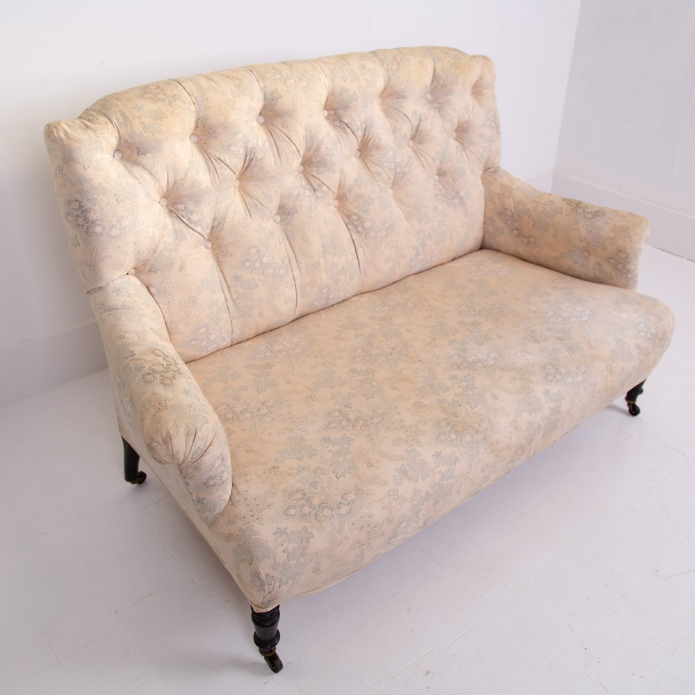 An antique French Napoleon III sofa upholstered in pale cream patterned fabric with deep buttoning, curved backrest, and turned dark wooden legs on brass castors. View VIII