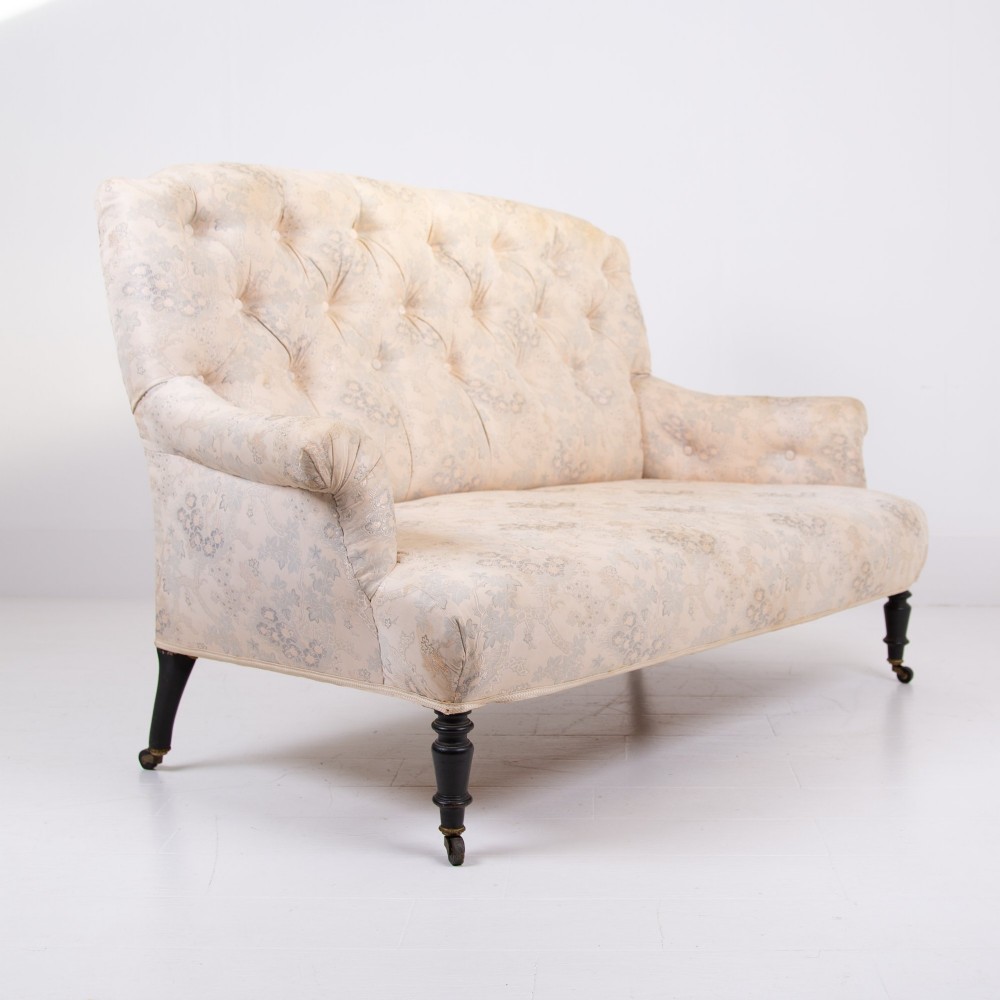 An antique French Napoleon III sofa upholstered in pale cream patterned fabric with deep buttoning, curved backrest, and turned dark wooden legs on brass castors. View IX