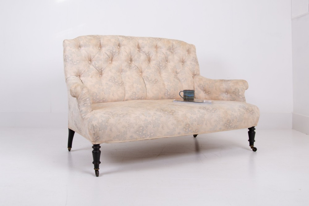 An antique French Napoleon III sofa upholstered in pale cream patterned fabric with deep buttoning, curved backrest, and turned dark wooden legs on brass castors. View XII
