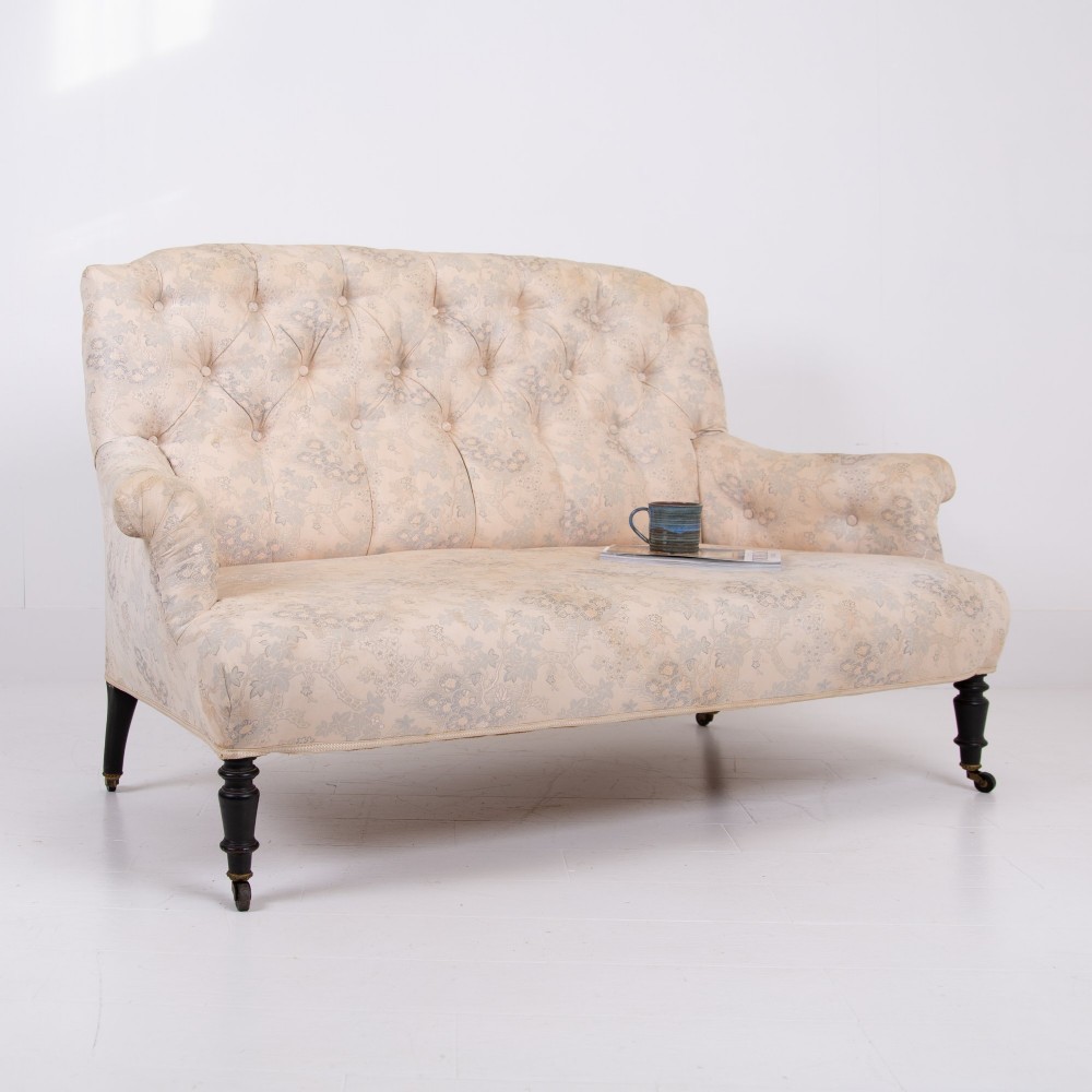 An antique French Napoleon III sofa upholstered in pale cream patterned fabric with deep buttoning, curved backrest, and turned dark wooden legs on brass castors. View XIII