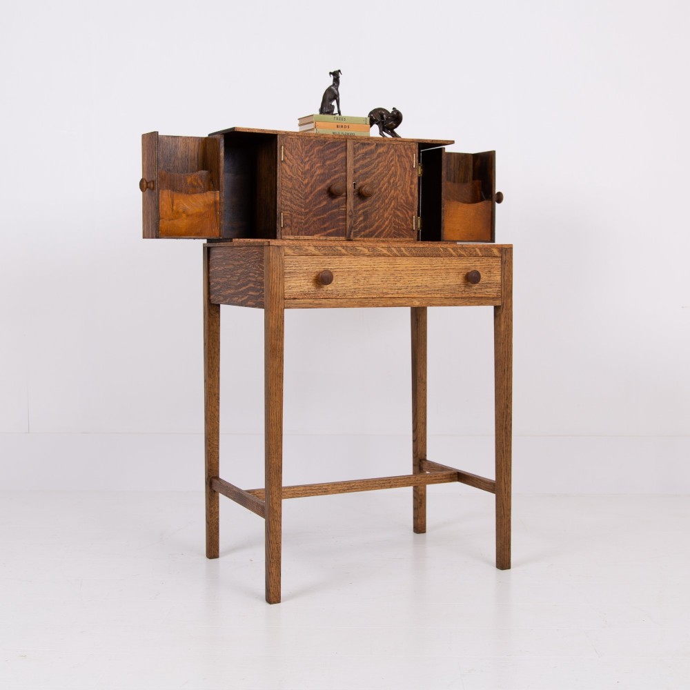 A 1930s warm brown oak writing desk featuring a top compartment with cupboard doors, side fold-out sections, and a single drawer on square legs.