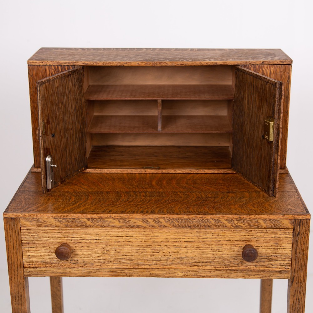 A 1930s warm brown oak writing desk featuring a top compartment with cupboard doors, side fold-out sections, and a single drawer on square legs. View V