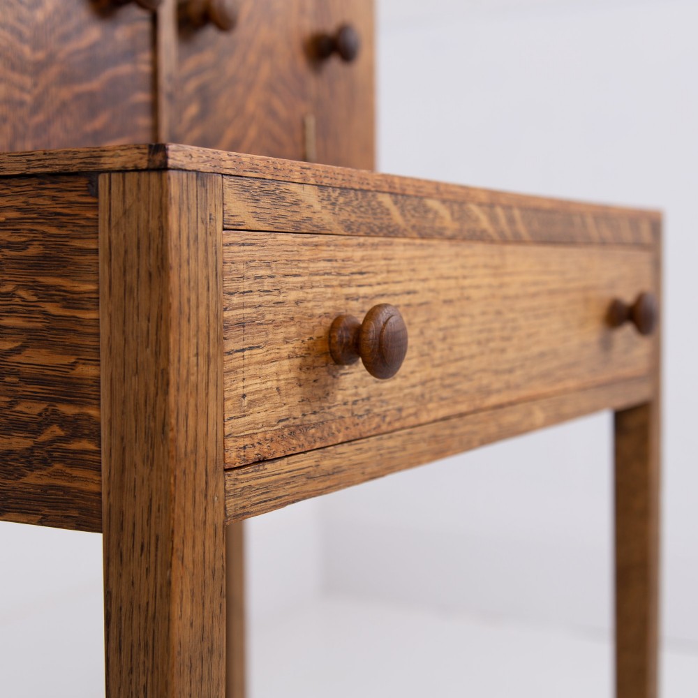 A 1930s warm brown oak writing desk featuring a top compartment with cupboard doors, side fold-out sections, and a single drawer on square legs. View X