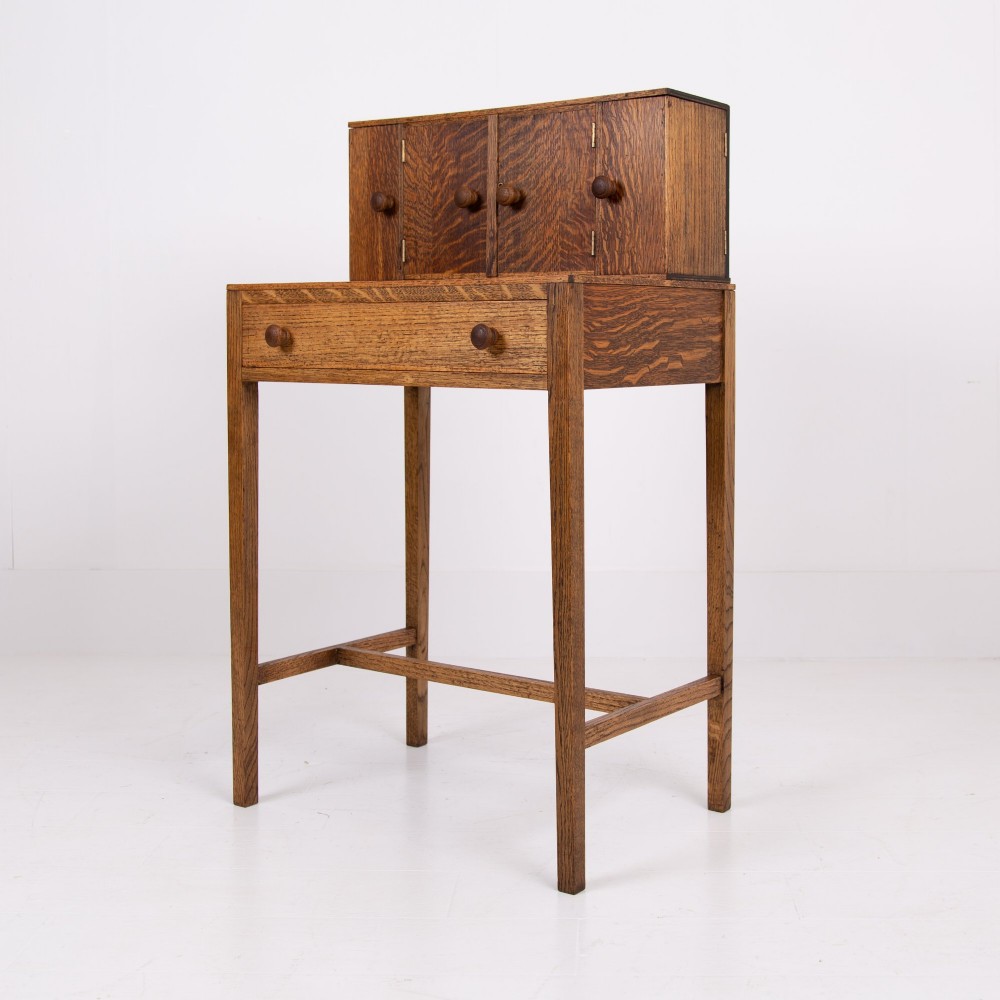 A 1930s warm brown oak writing desk featuring a top compartment with cupboard doors, side fold-out sections, and a single drawer on square legs. View XI