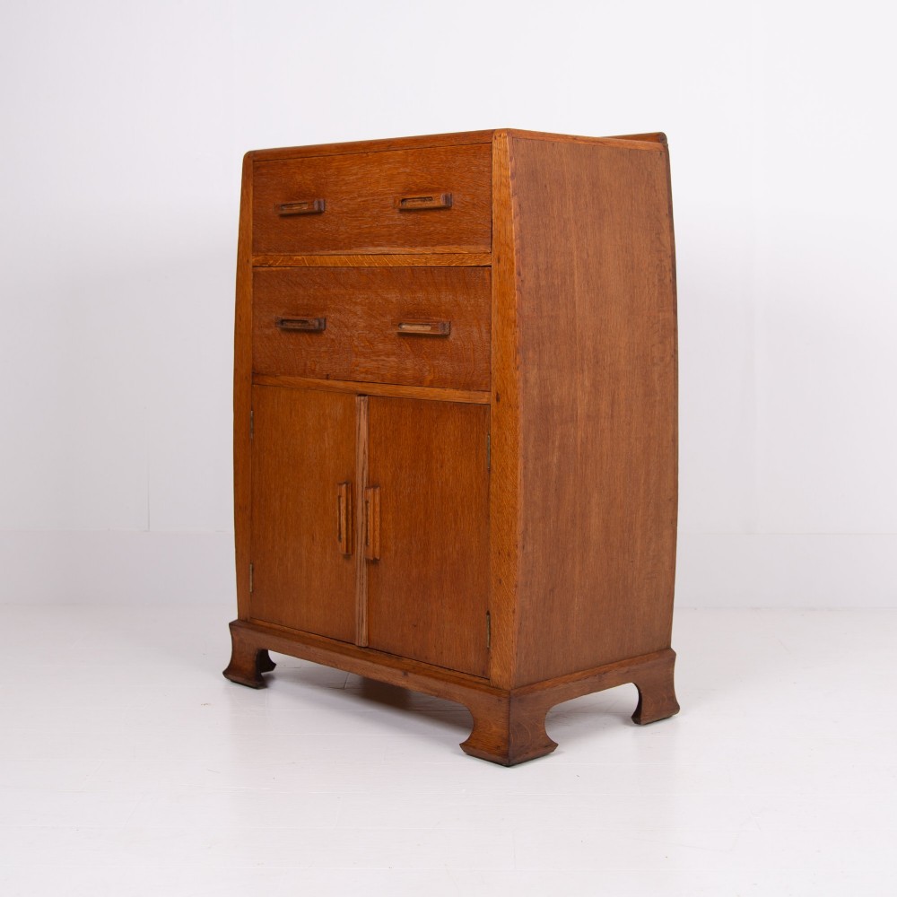 A 1930s Art Deco medium brown oak tallboy cabinet featuring two upper drawers with carved wooden handles and a double-door cupboard below.